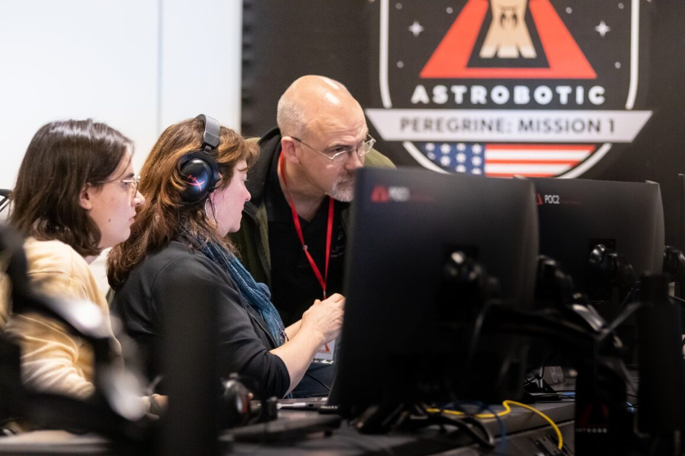 Three people looking at a computer monitor with an Astrobotic symbol in the background. 