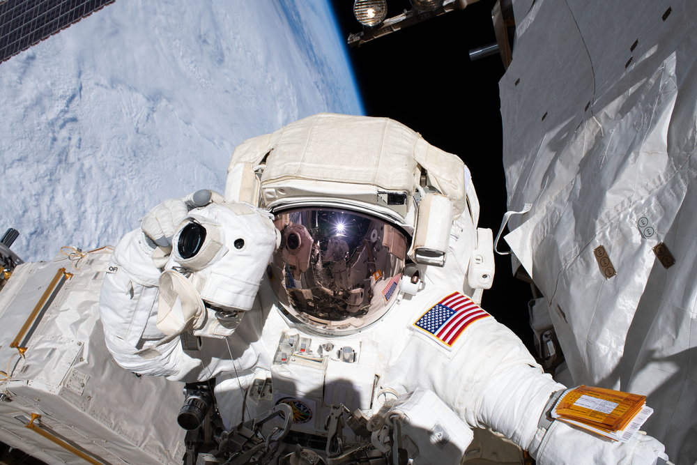 A person in a white space suit holding a camera during a spacewalk outside of the International Space Station.