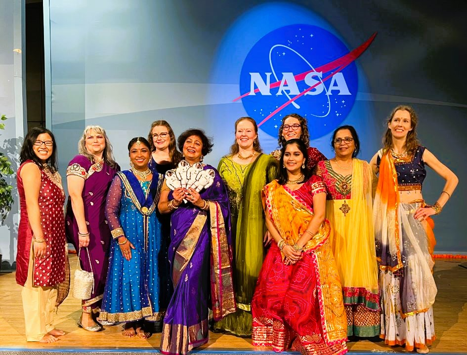 A group of ten people dressed in costumes in front of a blue background with a NASA logo.