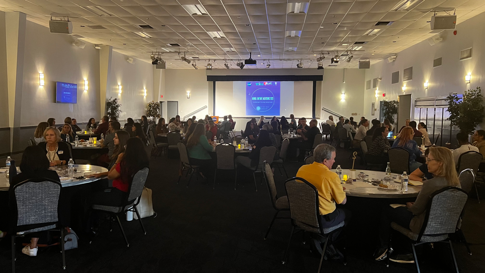 A group of people gathered in a conference room overlooking a projector with a blue screen. 