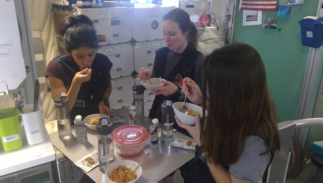 From left to right: Monique Garcia, Lauren Cornell, and Madelyne Willis — three members of the Human Exploration Research Analog Campaign 6 Mission 1 crew — gather around a small table to eat their lunch. Credits: NASA