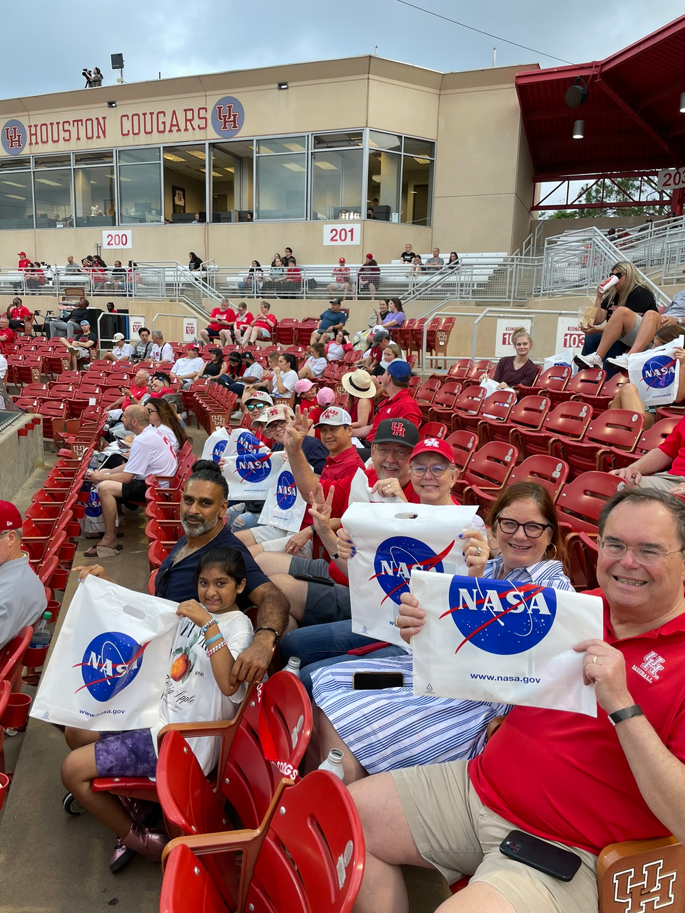 A group of people hold up white plastic bags with the NASA emblem on them in a large outdoor stadium. 