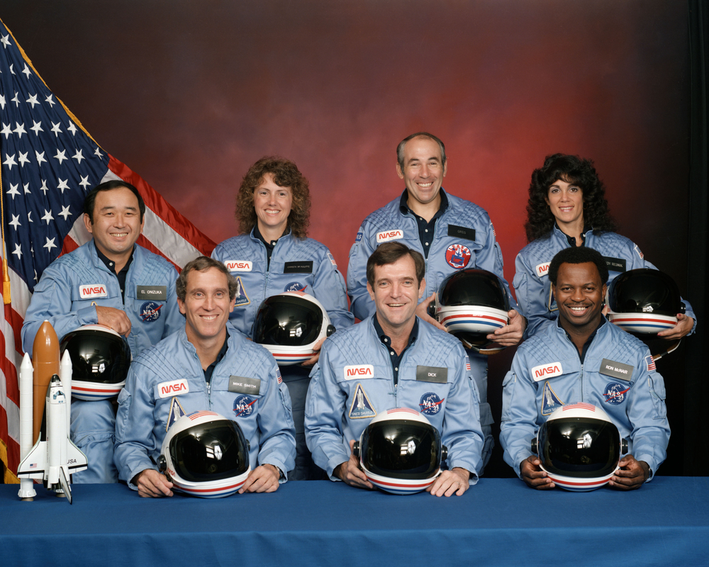 A group of seven people posing for a photo in front of an American flag. 