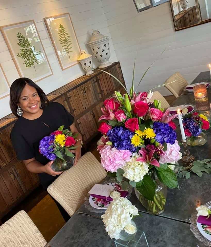 A person holding a bouquet of flowers beside a table full of flowers. 