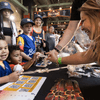 People pose for pictures and visit an informational booth during a baseball game.