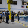 Images of a group of people filming inside of a facility containing a large pool.