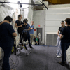 Images of a group of people filming inside of a facility containing a large pool.