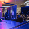 People gather together around a television in a cafeteria.