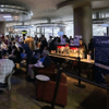 People gather together around a television in a cafeteria.