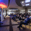 People gather together around a television in a cafeteria.