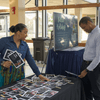 People gather in an auditorium lobby to explore exhibit tables.