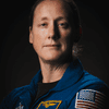 A person posing in a blue spacesuit in front of a black background. 