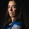 A person posing in a blue spacesuit in front of a black background. 