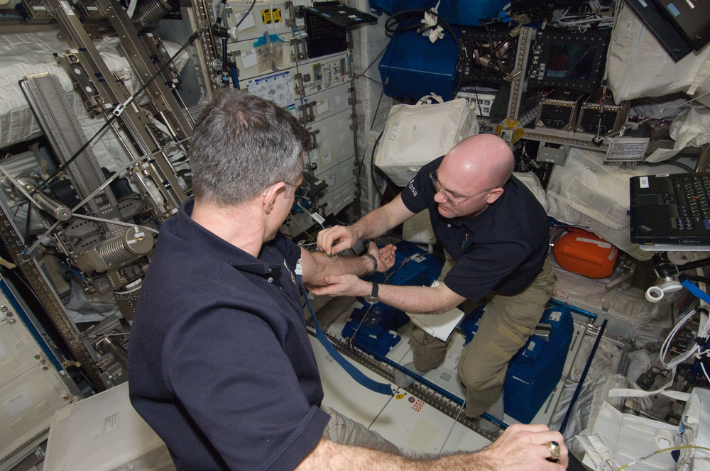 An astronaut draws a blood sample from another astronaut.