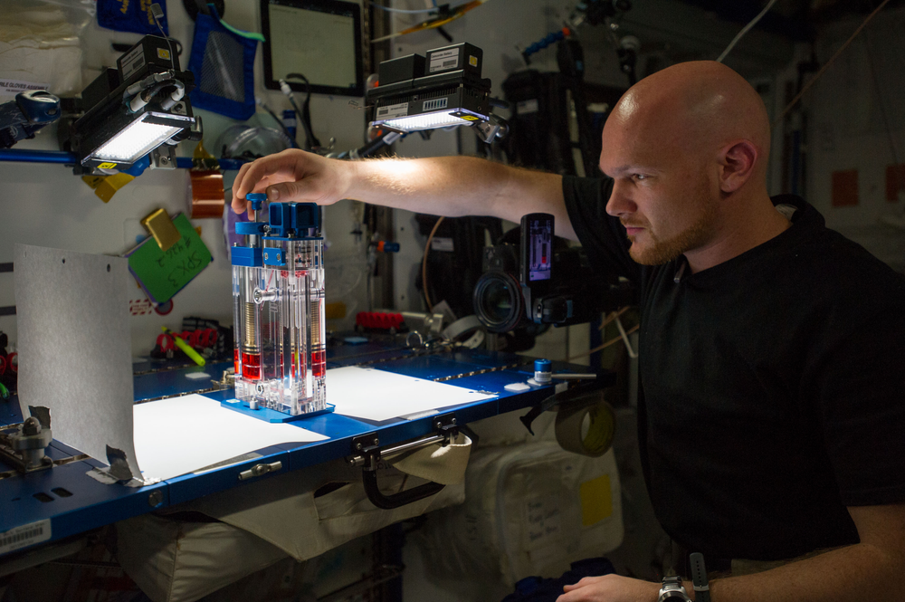 A man in a black shirt analyzes an experiment placed on a table in microgravity.