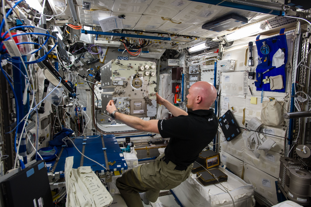 A bald man in a black shirt holding a piece of hardware aboard the International Space Station.