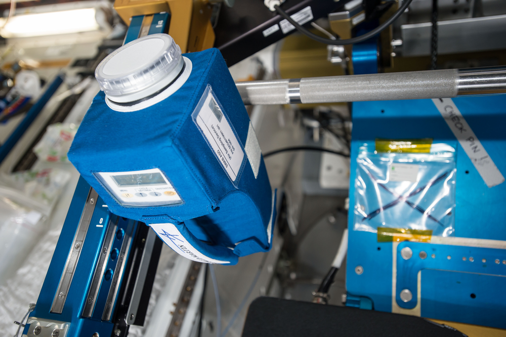 A blue and white sample collection container is shown on the International Space Station.