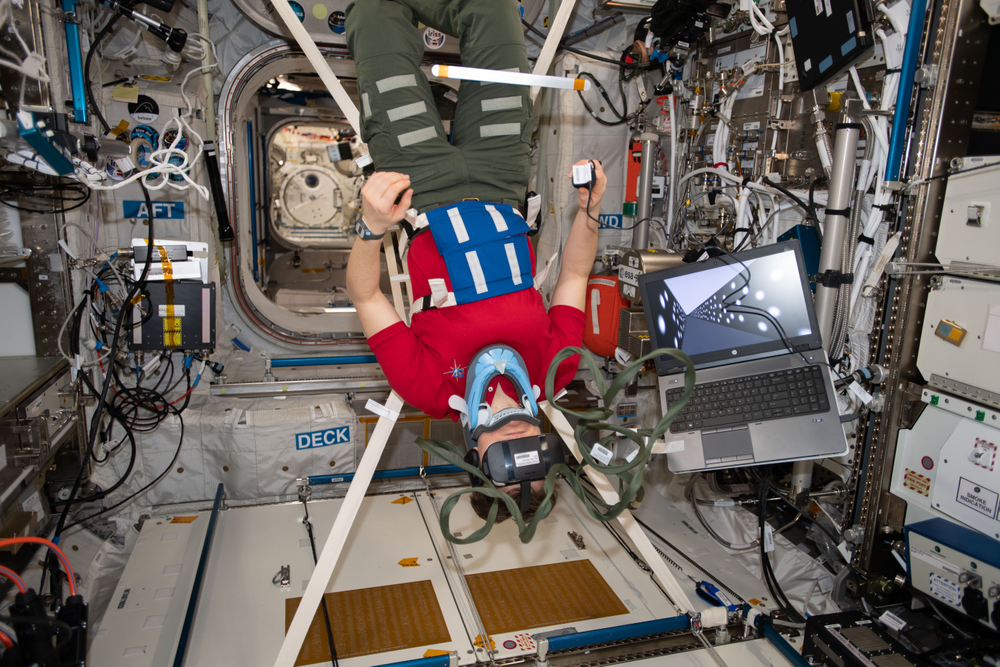 A person standing upside down wearing virtual reality goggles aboard the International Space Station. 