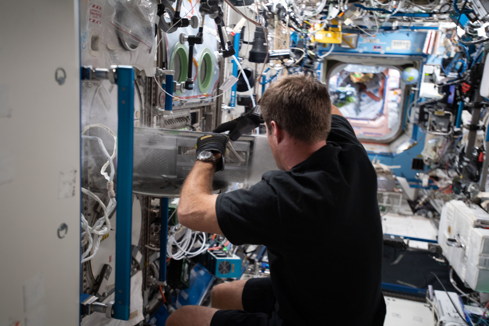 An astronaut floats as he places samples in a freezer aboard the International Space Station.