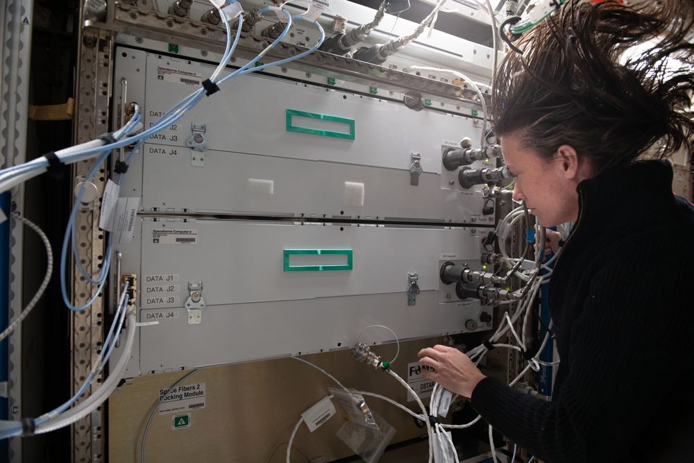 A person in microgravity wearing a black sweater in front of a space station module.