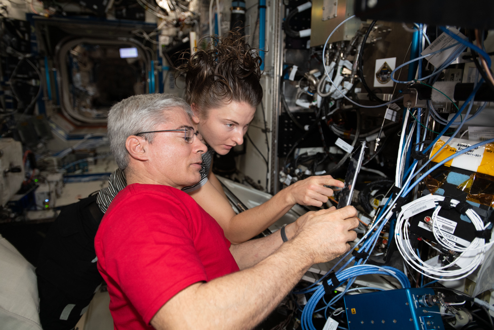 Two people conduct an experiment in microgravity aboard the International Space Station.