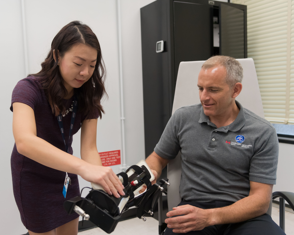 A person standing up is putting a device on another person's arm while they are sitting down