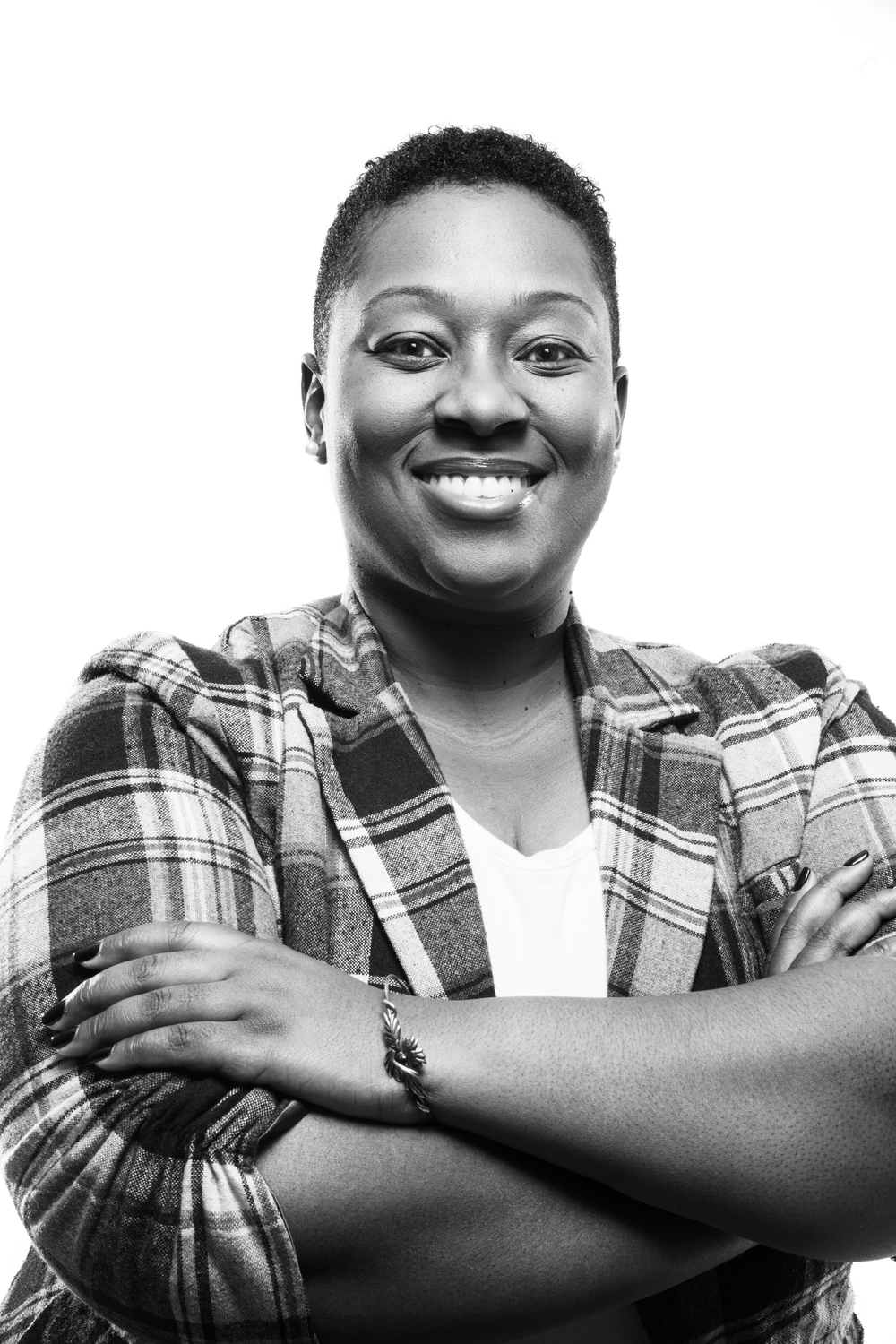 A person wearing a plaid shirt smiling with their arms folded in front of a white background.