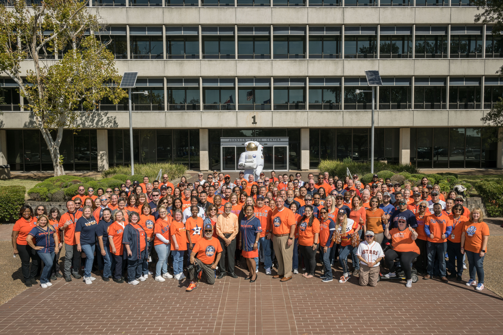 A group of people wearing orange shirts gathered outside in front of a building.