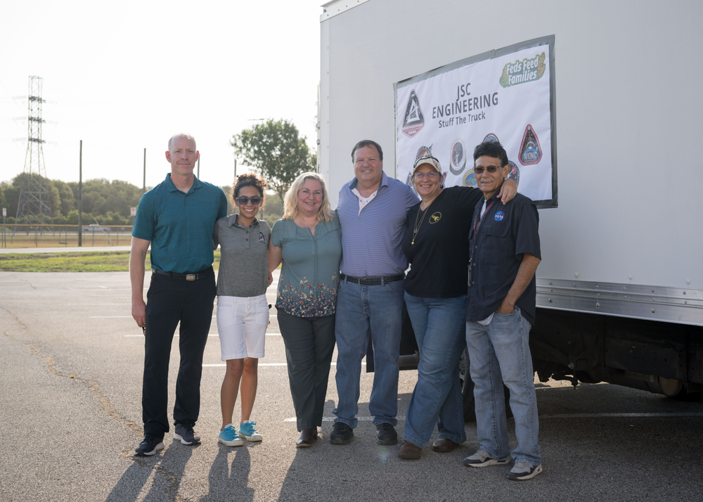 A group of men and women pose for a photo in front of a white delivery truck marked JSC Engineering Stuff the Truck.