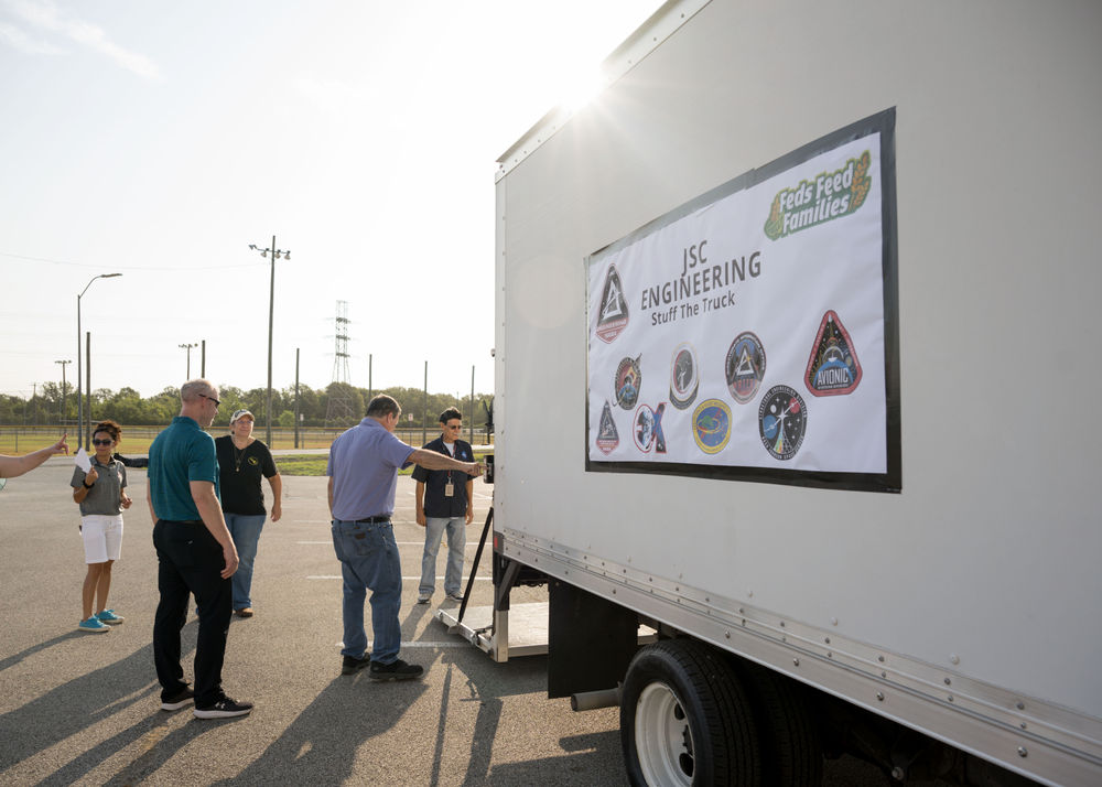 A group of people unloads a white delivery truck with a banner on the side reading JSC Engineering Stuff the Truck.