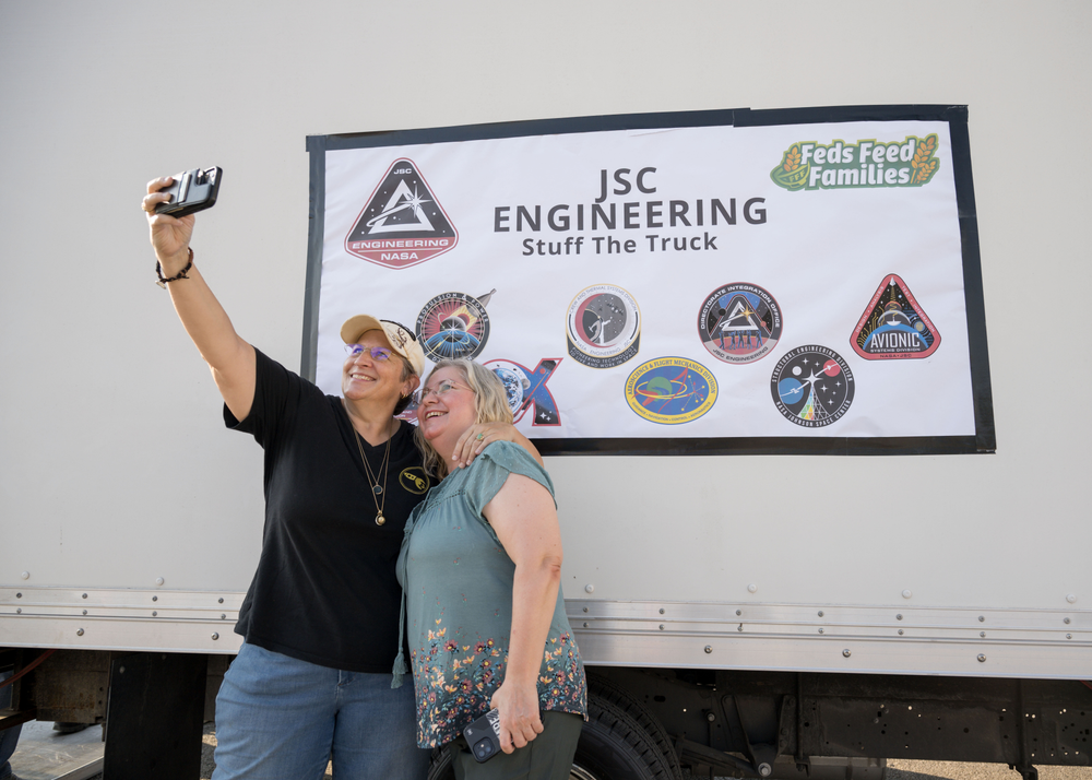 Two women pose for a selfie in front of a white delivery truck marked JSC Engineering Stuff the Truck.