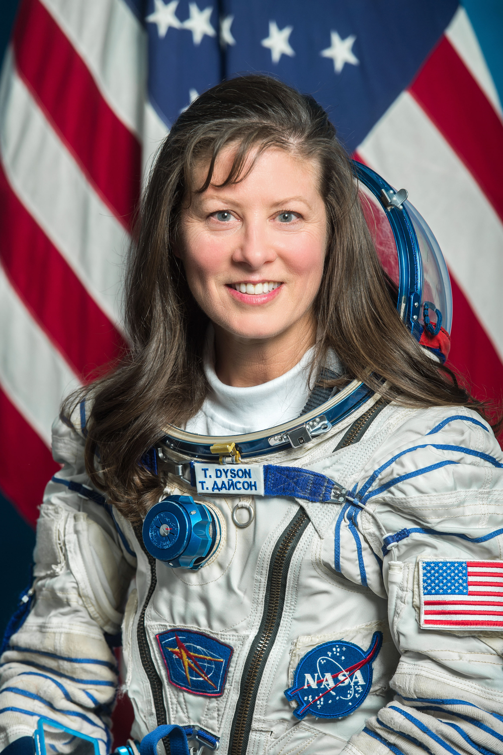 A female astronaut is pictured in a Russian spacesuit with an American flag in the background.
