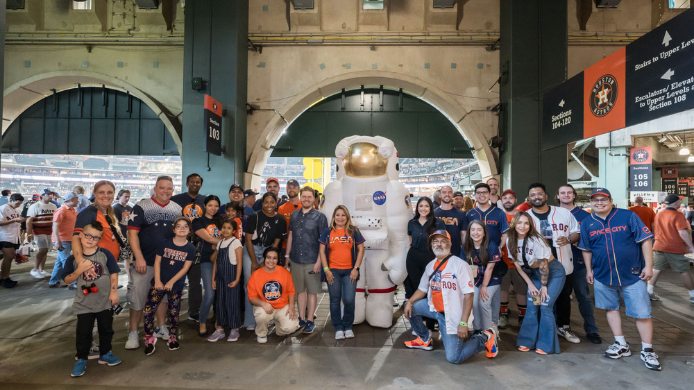 A group of people pose with an astronaut mascot at a baseball stadium.