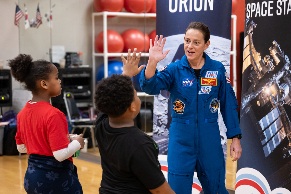 A person in a blue jumpsuit gives a high five to a child in a black shirt as a child in a red shirt watches. 