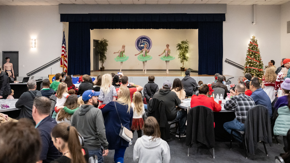 Three people in green tutus dance on stage in front of an audience. 