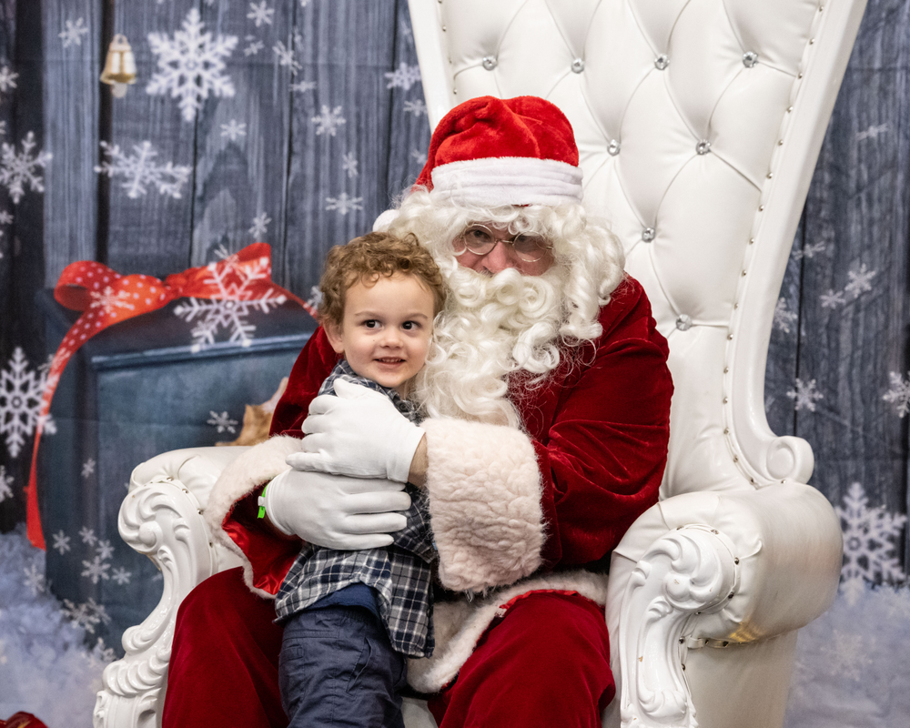 Santa sits in a white chair and holds a child in his lap.