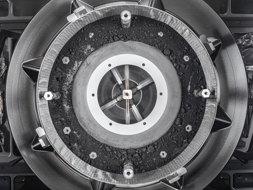 The inside of an asteroid sample collection canister is shown, with rocks, dust, and other pieces visible.