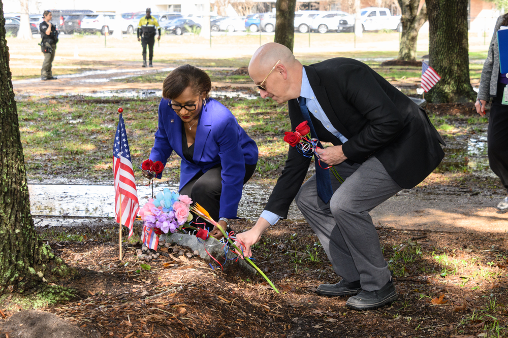 Two people placing roses on a memorial under a tree.