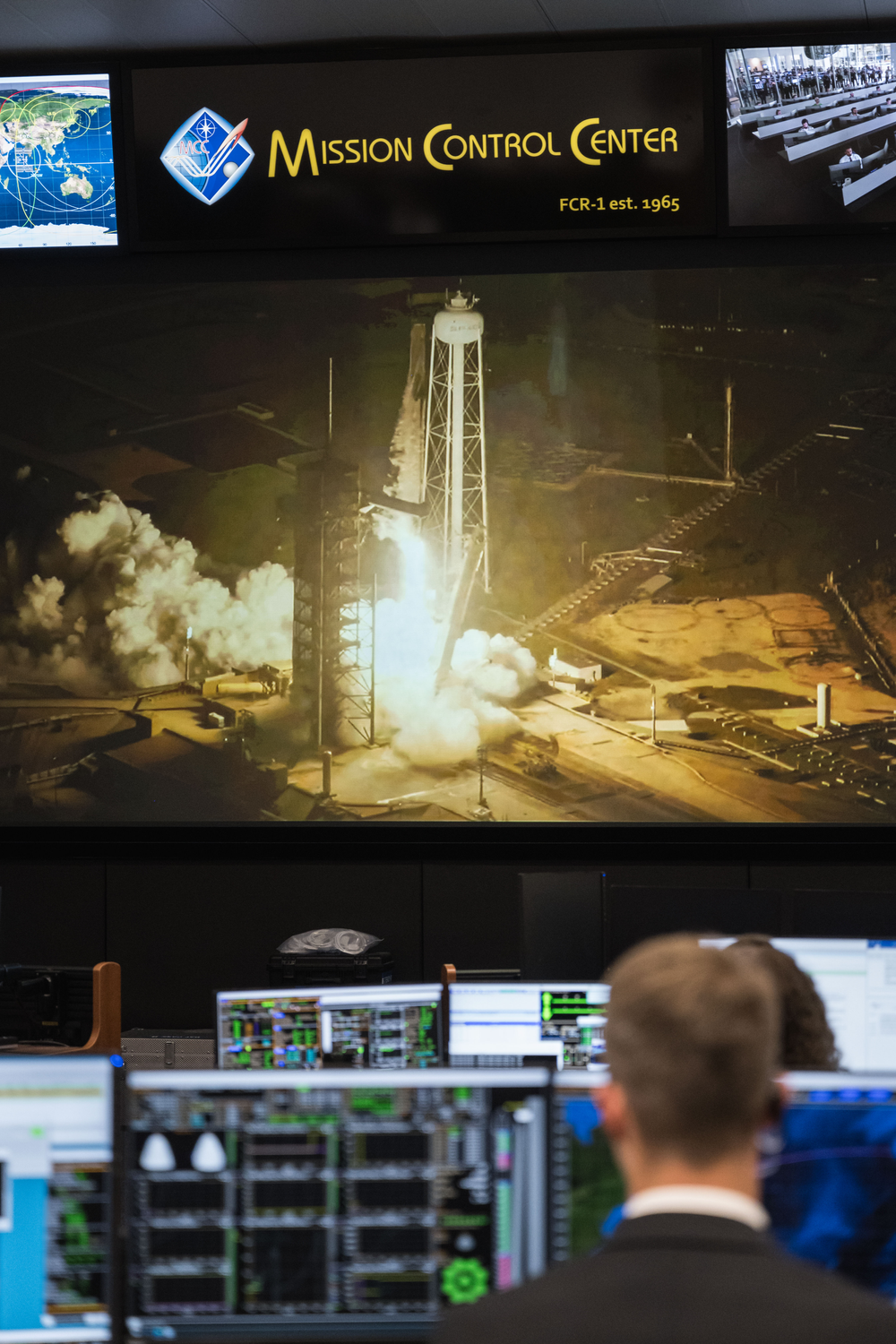 A back view of a person watching a launch on a big screen. 