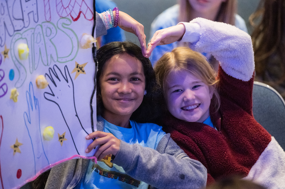 Children hold up posters in a crowded auditorium. 