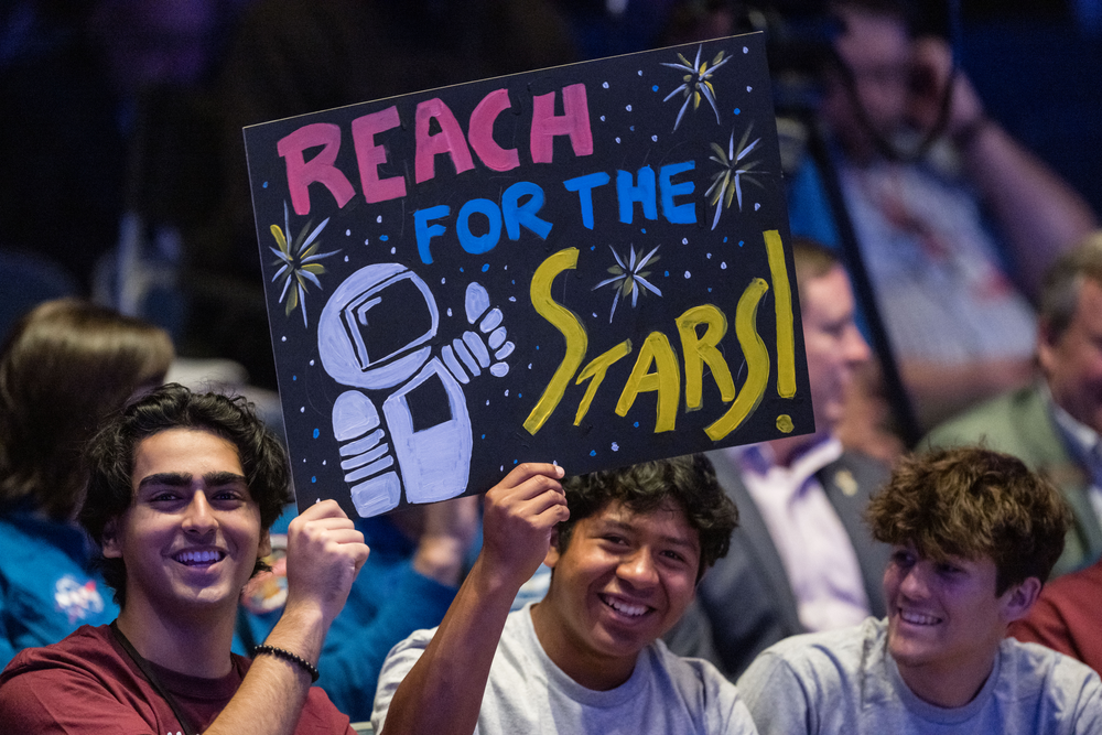 Children hold up posters in a crowded auditorium. 