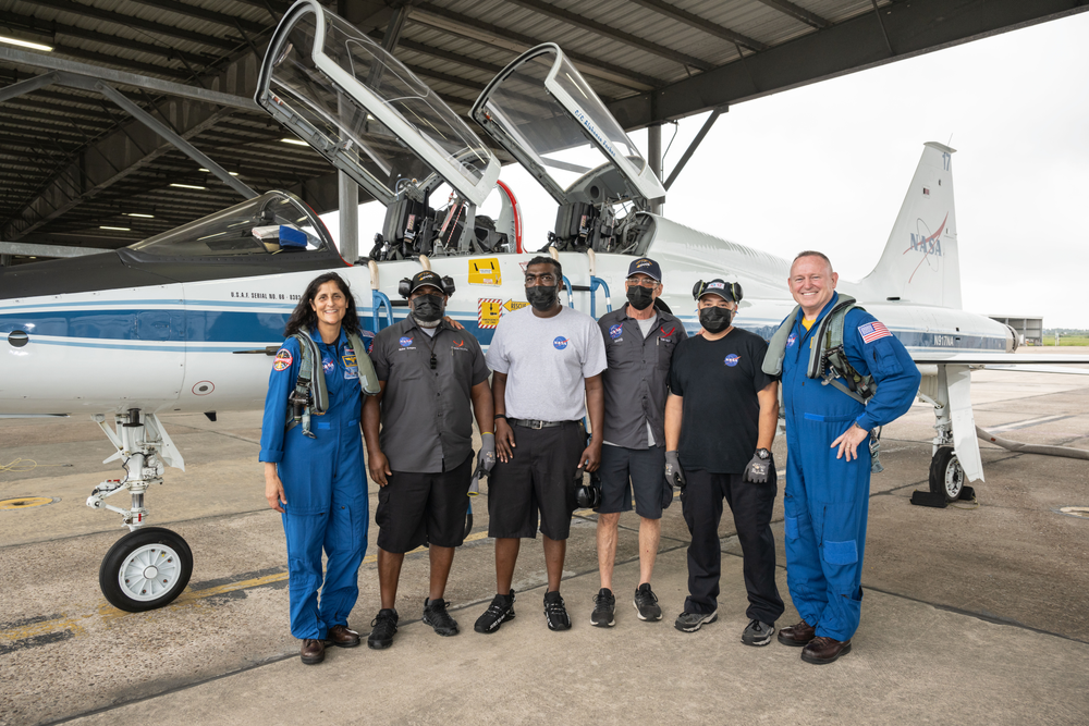 Two astronauts in blue flight suits pose for a picture with airfield ground crew members in front of a T-38 jet.