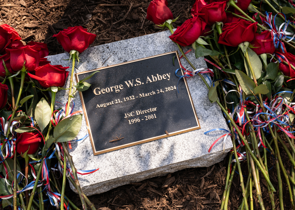 A memorial stone for George W.S. Abbey is surrounded by roses.