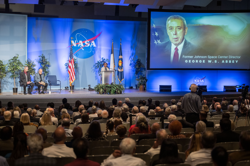 NASA leaders speak to a large audience in an auditorium during a memorial service.