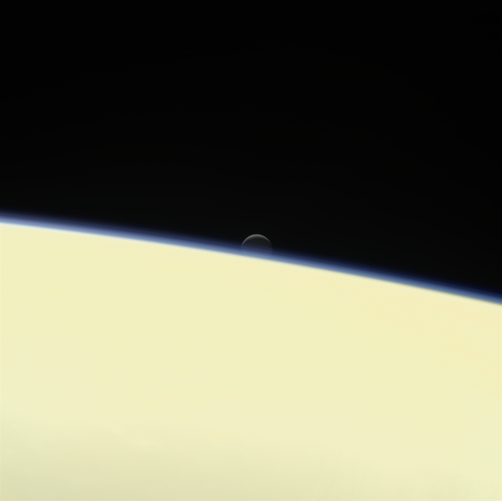 Saturn's active, ocean-bearing moon Enceladus sinks behind the giant planet in a farewell portrait from NASA's Cassini spacecraft.
