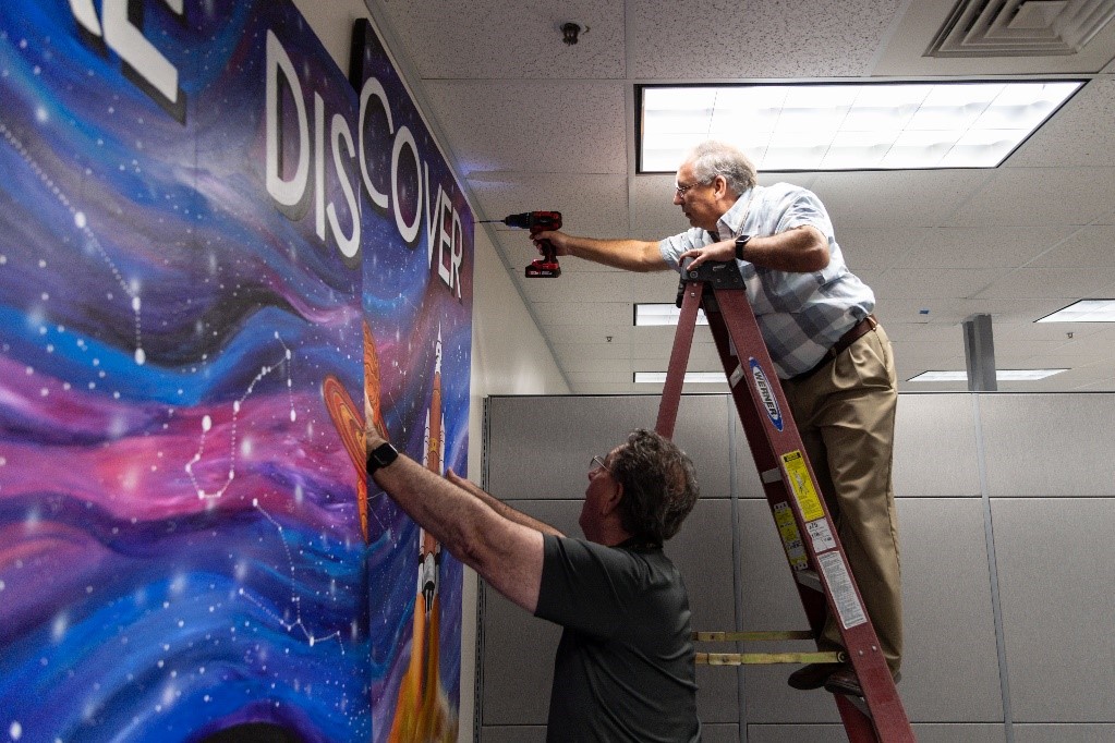 Gary Johnson and Raul Tijerina install the first mural panel. Credits: NASA/Joshua Valcarcel