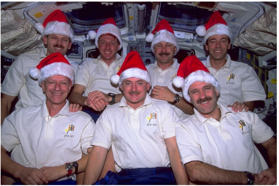 The STS-103 crew of (from left front) Claude Nicollier, Scott J. Kelly, and John M. Grunsfeld; (front left rear) Steven L. Smith, C. Michael Foale, Curtis L. Brown, and Jean- François A. Clervoy, showing off their Santa hats on the flight deck of space shuttle Discovery in 1999. Credits: NASA