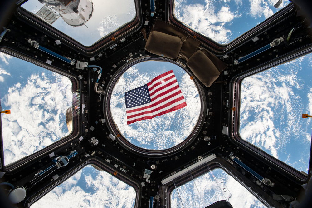 A portrait of the American flag floating in the International Space Station's cupola with Earth in the background. 