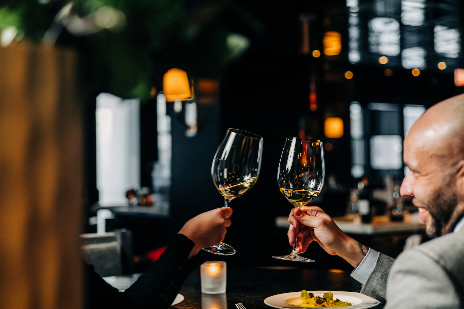 Two people’s hands cheersing two glasses of white wine.