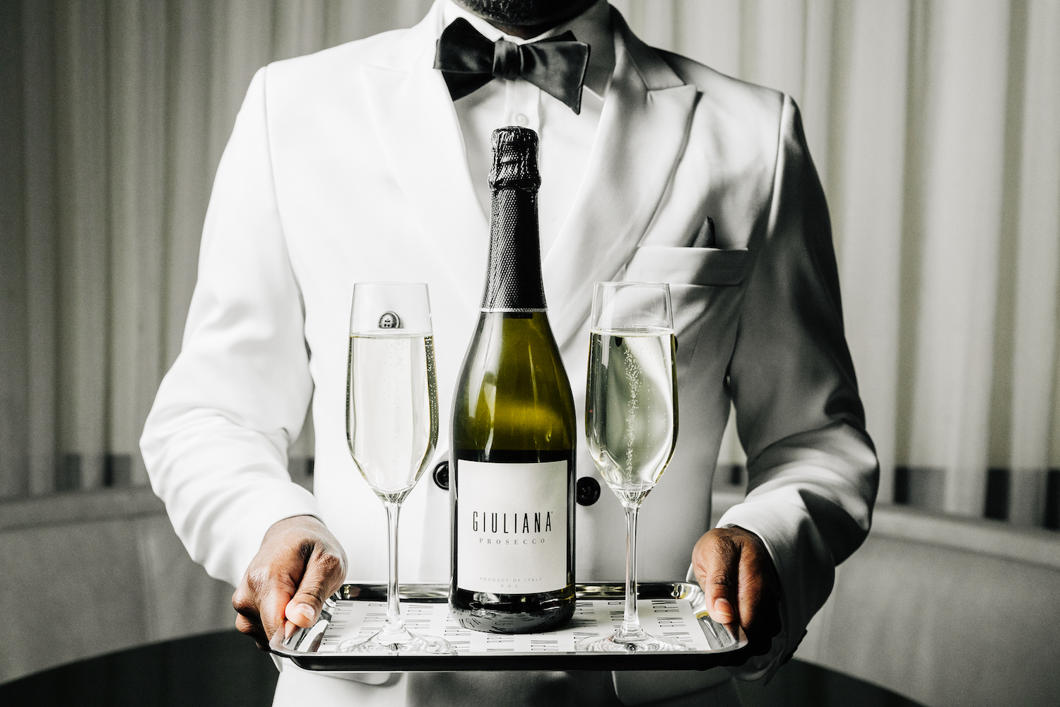 man holding a tray with a bottle of Giuliana Prosecco and two champagne flutes